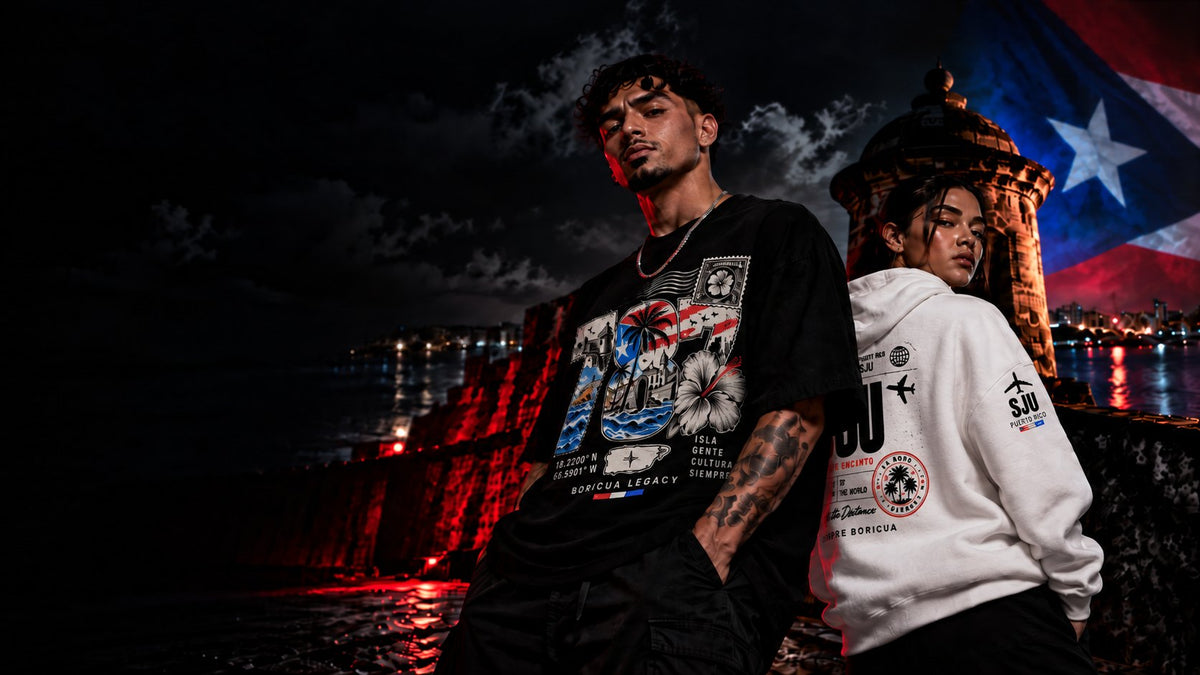 Two models wearing Boricua Legacy Puerto Rican streetwear at night in Old San Juan beside a garita with the Puerto Rican flag lit behind them.